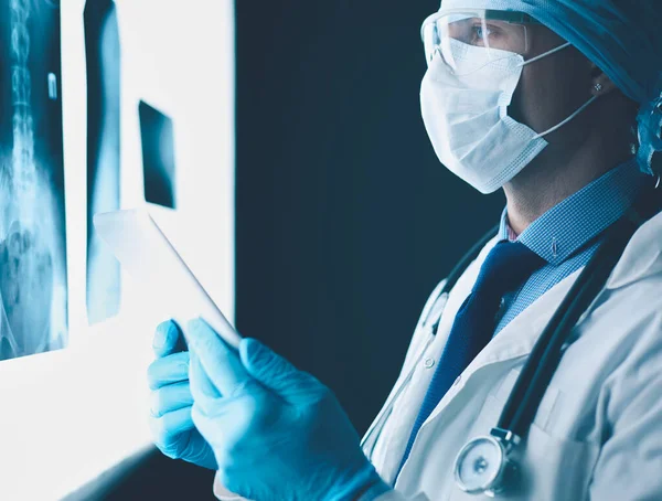 Médecin à l'hôpital assis au bureau regardant les rayons X sur tablette sur fond blanc avec des rayons X — Photo