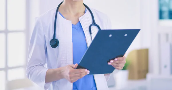 Giovane sorridente medico femminile con stetoscopio in possesso di una cartella presso lo studio medico — Foto Stock