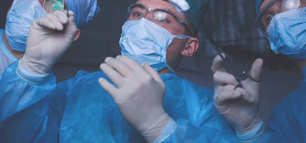 Grupo de cirurgiões no trabalho em sala de operações tonificada em azul. Equipe médica realizando operação — Fotografia de Stock