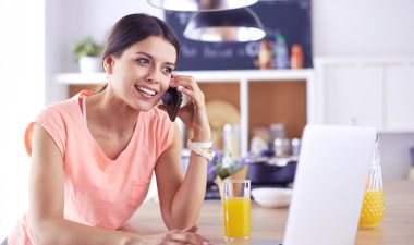 Mutfakta dizüstü bilgisayara benzeyen tariflerle gülümseyen genç bir kadın. Gıda blogcusu kavramı