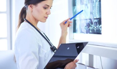 Stetoskop lu genç gülümseyen kadın doktor doktor ofisinde röntgeni işaret ediyor