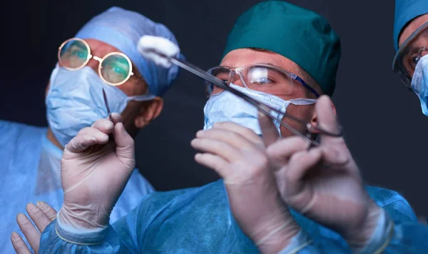 Grupo de cirurgiões no trabalho em sala de operações tonificada em azul. Equipe médica realizando operação — Fotografia de Stock