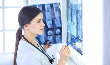 Stetoskop lu genç gülümseyen kadın doktor doktor ofisinde röntgeni işaret ediyor