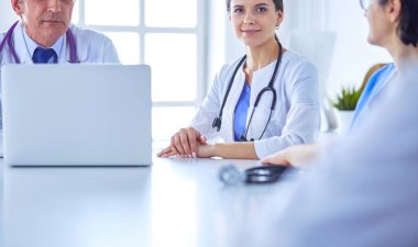 Ciddi bir tıbbi ekip, parlak bir danışma odasında dizüstü bilgisayar kullanıyor.