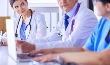 Parlak bir hastane odasında meslektaşlarıyla çalışan gülümseyen bir doktor.