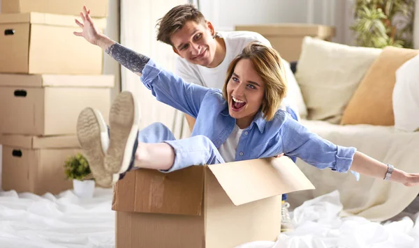 Gelukkig paar hebben plezier en paardrijden in kartonnen dozen in nieuwe huis — Stockfoto