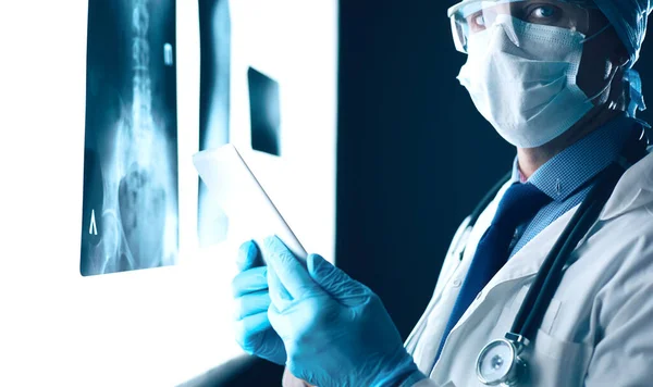 Doctor in hospital sitting at desk looking at x-rays on tablet against white background with x-rays — Stock Photo, Image