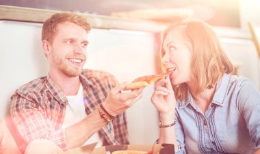 Genç çift, yeni bir eve taşındıktan sonra etraflarında kutularla yerde pizza molası veriyorlar. Genç çift