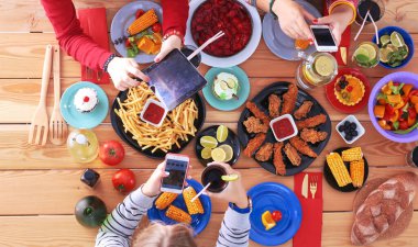 Ahşap masada otururken birlikte yemek yiyen bir grup insanın üst düzey görüntüsü. Masada yemek var. İnsanlar fast food yiyor..