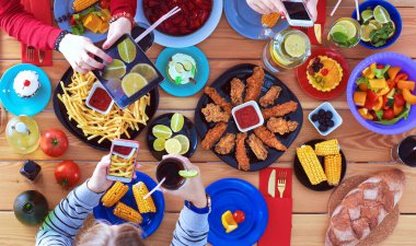 Ahşap masada otururken birlikte yemek yiyen bir grup insanın üst düzey görüntüsü. Masada yemek var. İnsanlar fast food yiyor..