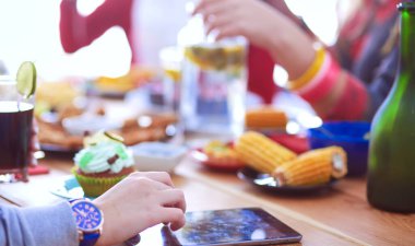 Ahşap masada otururken birlikte yemek yiyen bir grup insanın üst düzey görüntüsü. Masada yemek var. İnsanlar fast food yiyor..
