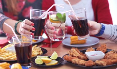 Ahşap masada otururken birlikte yemek yiyen bir grup insanın üst düzey görüntüsü. Masada yemek var. İnsanlar fast food yiyor..