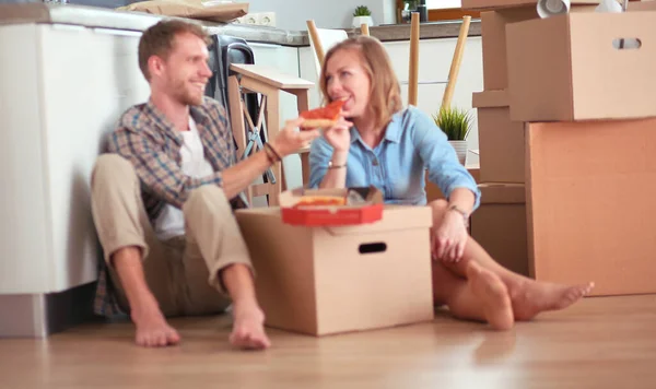 Giovani coppie hanno una pausa pranzo pizza sul pavimento dopo essersi trasferiti in una nuova casa con scatole intorno a loro. Coppia giovane — Foto Stock