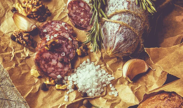 Ιταλικό σαλάμι με θαλασσινό αλάτι, δενδρολίβανο, σκόρδο και ξηρούς καρπούς σε χαρτί. Ρουστίκ στυλ. Κλείσε.. — Φωτογραφία Αρχείου