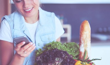 Mutfakta cep telefonu taşıyan gülümseyen bir kadın.