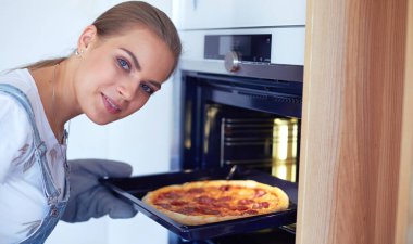 Mutlu genç bayan evde pizza pişiriyor.