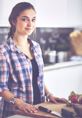 Masanın yanındaki mutfakta sebze doğrayan genç bir kadın.