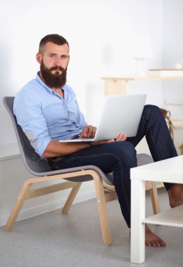 Yakışıklı genç adam dizüstü bilgisayarda oturuyor ve çalışıyor..