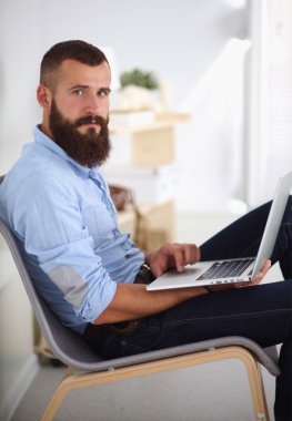 Yakışıklı genç adam dizüstü bilgisayarda oturuyor ve çalışıyor..