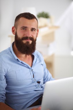 Yakışıklı genç adam dizüstü bilgisayarda oturuyor ve çalışıyor..