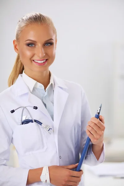 हॉस्पिटलमध्ये एकसमान उभे असलेल्या फोल्डरसह स्मित महिला डॉक्टर — स्टॉक फोटो, इमेज