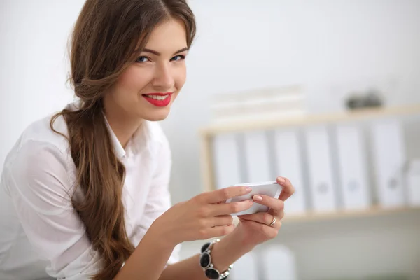 Businesswoman sending message with smartphone sitting in the of — Stock Photo, Image