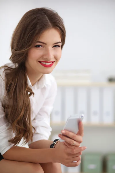 Businesswoman sending message with smartphone sitting in the of — Stock Photo, Image