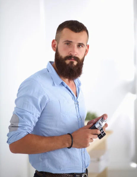 Joven barba hombre sosteniendo una cámara mientras está de pie contra blanco b — Foto de Stock