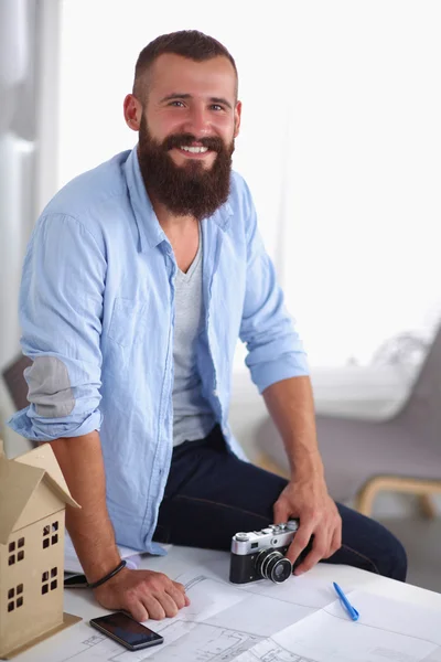 Portret van mannelijke ontwerper zittend op een tafel met blauwdrukken een — Stockfoto
