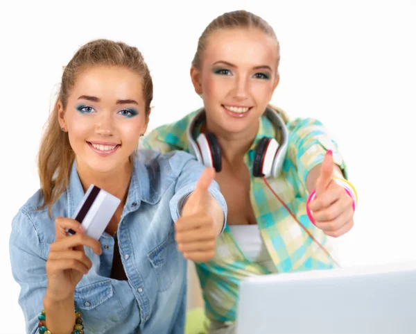 Duas mulheres jovens sentadas com laptop e carrinho de crédito mostrando ok — Fotografia de Stock