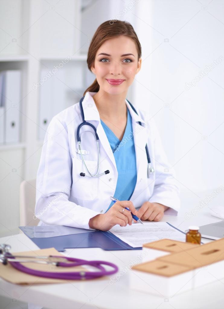 Beautiful young smiling female doctor sitting at the desk and w