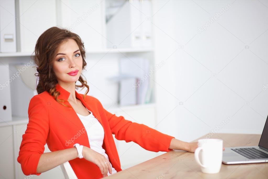 Attractive woman sitting at desk in office, working with laptop