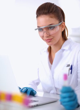 Kadın araştırmacı, beyaz arka planda izole edilmiş ilaç şişeleri ve mataralarla çevrili.