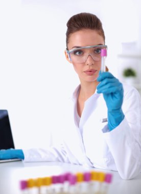 Kadın araştırmacı, beyaz arka planda izole edilmiş ilaç şişeleri ve mataralarla çevrili.