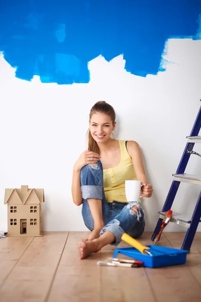 Portret malarza kobieta siedzi na podłodze w pobliżu ściany po paintingand trzymając kubek — Zdjęcie stockowe