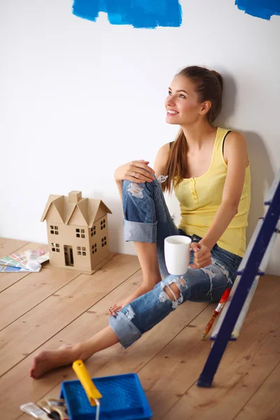 Portret malarza kobieta siedzi na podłodze w pobliżu ściany po paintingand trzymając kubek — Zdjęcie stockowe