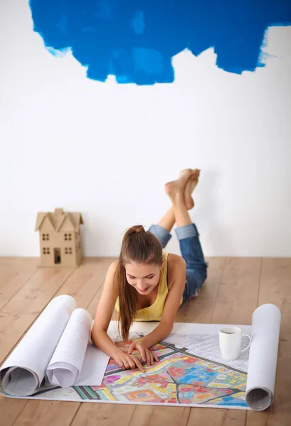 ผู้หญิงสาวนอนอยู่บนพื้นและมองไปที่พิมพ์เขียวของบ้านใหม่ — ภาพถ่ายสต็อก
