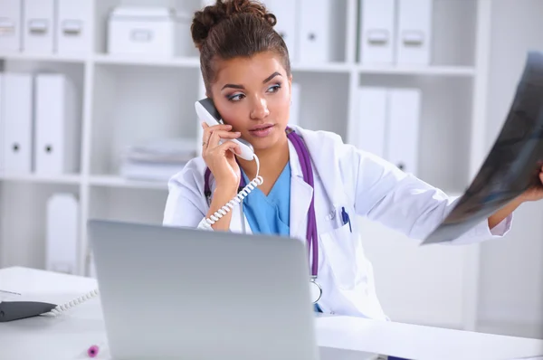 Médecin féminin regardant radiographie et parlant au téléphone dans le centre de diagnostic, assis au bureau — Photo