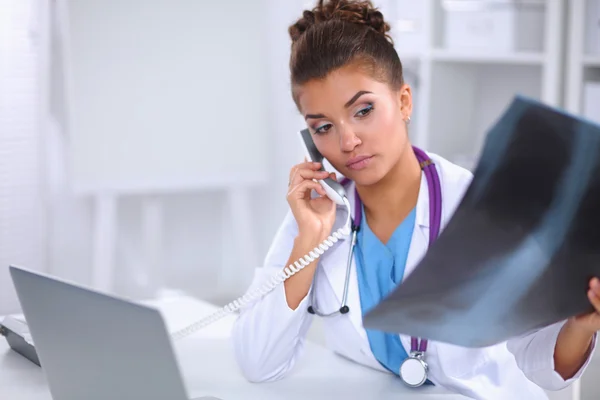 Médica olhando radiografia e falando por telefone no centro de diagnóstico, sentada na mesa — Fotografia de Stock