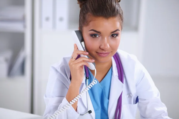 Médica feminina conversando por telefone no centro de diagnóstico, sentada na mesa — Fotografia de Stock