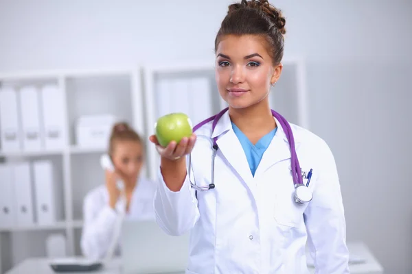 一位女医生手拿着一个绿色的苹果，站在办公室 — 图库照片