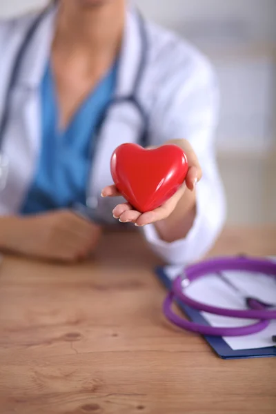 लाल दिल प्रतीक के साथ युवा डॉक्टर डेस्क पर बैठे अलग — स्टॉक फ़ोटो, इमेज