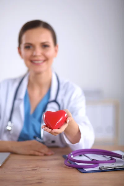 Jonge arts met rood hartsymbool aan bureau geïsoleerd — Stockfoto