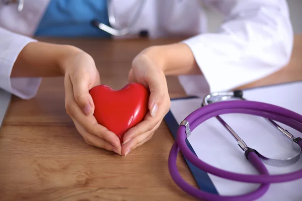 Joven médico con el símbolo del corazón rojo sentado en el escritorio aislado — Foto de Stock