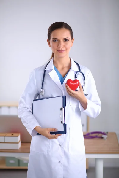 Νεαρή γυναίκα γιατρός κρατώντας φάκελο και μια κόκκινη καρδιά, απομονώνονται σε λευκό φόντο — Φωτογραφία Αρχείου