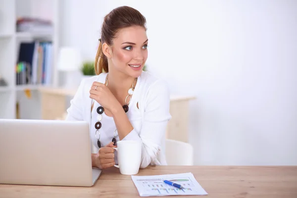 Jonge zakenvrouw zit op het bureau met beker in het kantoor — Stockfoto