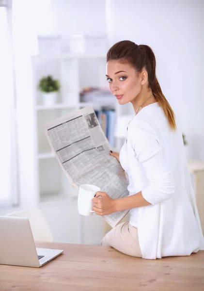 Cute businesswoman holding newspaper sitting at her desk in bright office — Stock Photo, Image