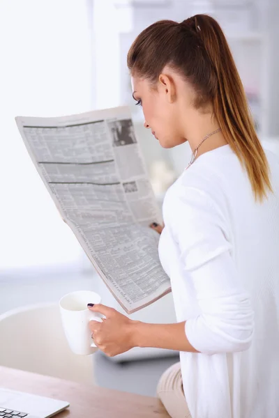 明るいオフィスで彼女の机に座って新聞を保持しているかわいい実業家 — ストック写真