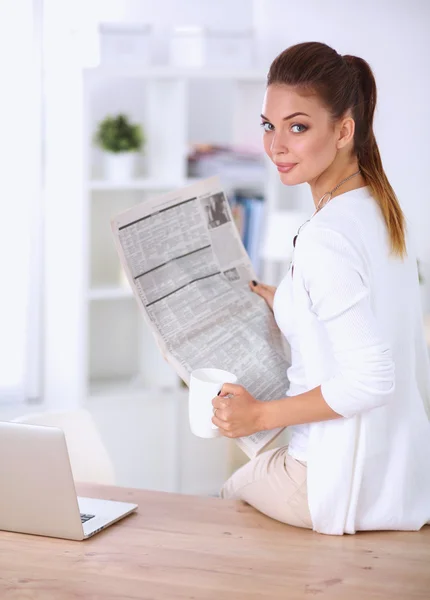 明るいオフィスで彼女の机に座って新聞を保持しているかわいい実業家 — ストック写真