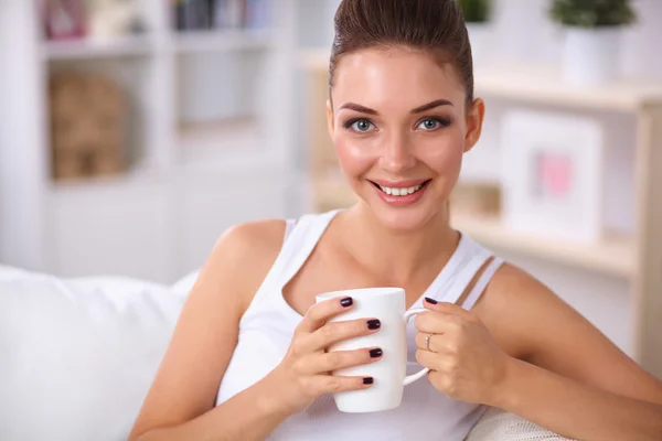 Young beautiful woman with a cup on sofa at home — Stock Photo, Image